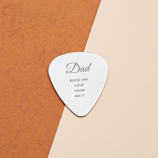 Silver guitar pick with 'Dad' and 'Love from Matt' text on a brown and beige background