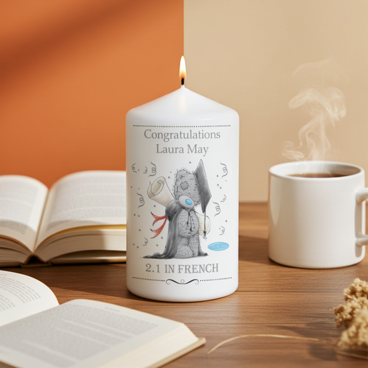 White candle with text and graphics on a wooden surface with books and a mug.