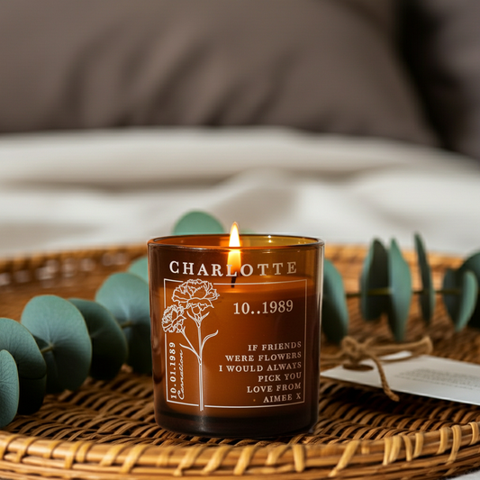 A personalized amber glass jar candle with a lit flame, featuring the name 'CHARLOTTE', the date '10.05.