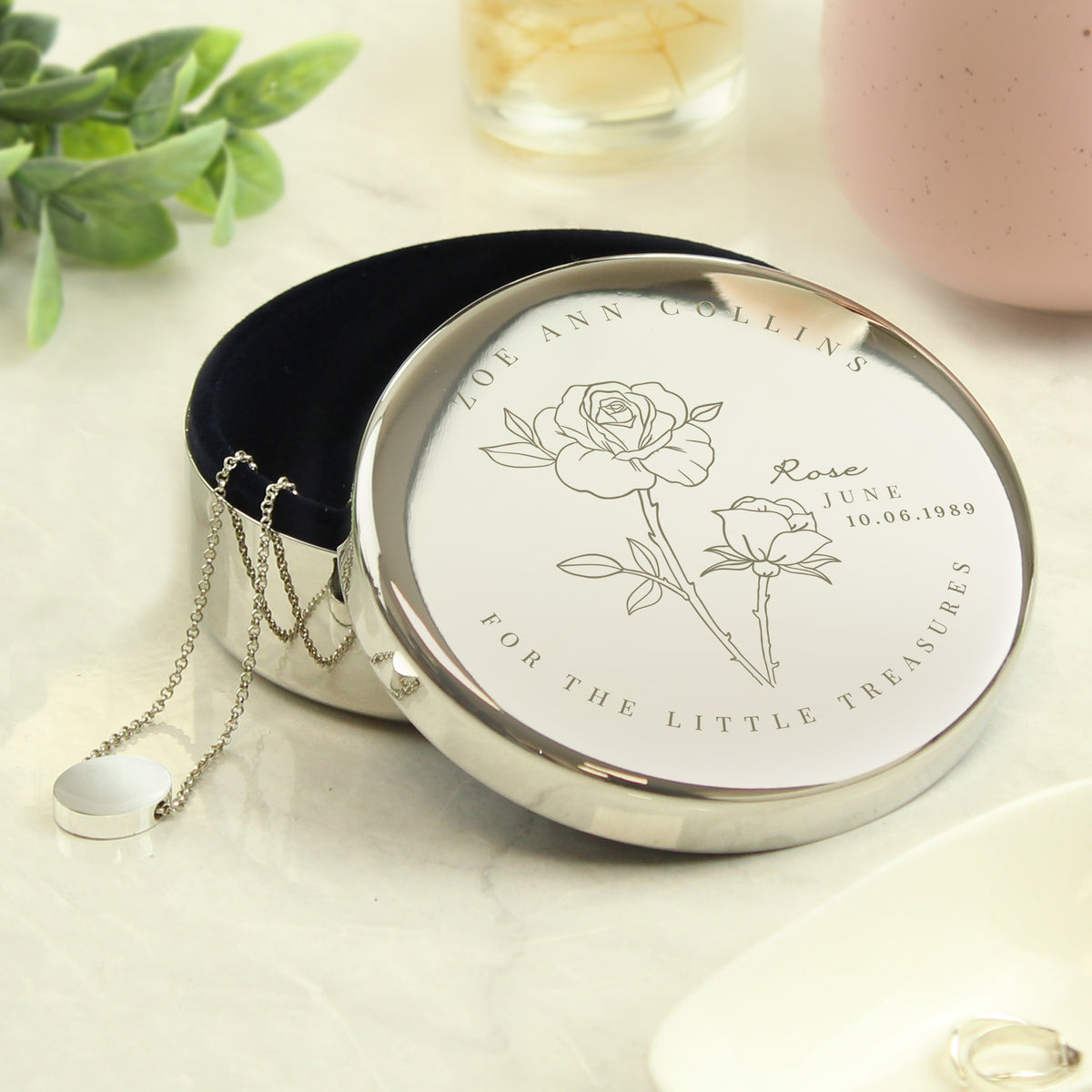 Silver necklace with engraved design in a round container on a light surface.