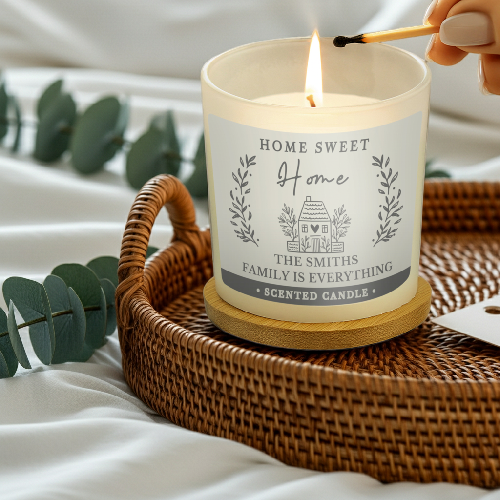 A lit cream-colored scented candle in a white glass jar sits on a wooden coaster inside a woven wicker tray. A hand holds a lit match near the flame.