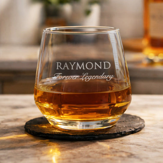 Glass of whiskey with 'RAYMOND Forever Legendary' engraving on a wooden surface.