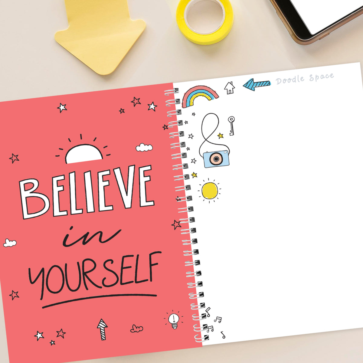 Notebook with 'Believe in Yourself' on pink cover, surrounded by stationery items.