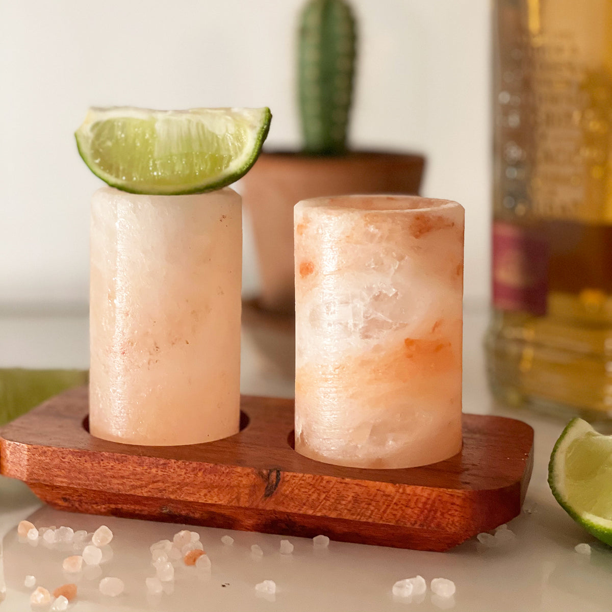 A set of 2 Himalayan salt shot glasses on a wooden tray, with each glass containing a small amount of pink Himalayan salt. '.